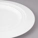 A close-up of a white Bon Chef Concentrics charger plate with a rim.
