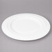 A white Bon Chef porcelain charger plate with a rim on a gray surface.
