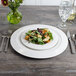 A Bon Chef white porcelain charger plate with a salad on a table.