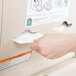 A hand using a Koala Kare baby changing station to put a diaper in a white Koala Kare diaper dispenser.