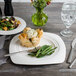 A white porcelain Bon Chef soft square dinner plate with a green salad on a table.