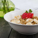 A white Bon Chef porcelain bowl filled with oatmeal, strawberries, and banana slices.