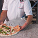 A person using a GI Metal square perforated pizza peel to remove a pizza from an oven.