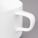 A close-up of a Bon Chef white porcelain cup with a slanted oval shape and handle.