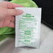 A hand holding a white packet with green text.