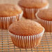 A close-up of a muffin and a cupcake in white fluted wrappers on a cooling rack.