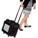 A woman in a skirt and blouse pulling a black bag with wheels similar to a suitcase.