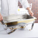 A chef using a Vollrath stainless steel water pan to prepare a large chafing dish.