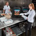 Two women in chef's uniforms using a Cambro front loading food pan carrier to store food in containers.