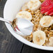 A Walco Pacific Rim stainless steel teaspoon in a bowl of oatmeal with bananas and strawberries.