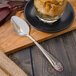 A Walco stainless steel dessert spoon on a wooden tray with a glass of dessert.