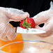 A gloved hand uses a Mercer Culinary Praxis paring knife to cut a strawberry.
