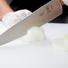 A person using a Mercer Culinary Praxis chef's knife to slice a white onion on a counter.