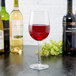 A Reserve by Libbey wine glass filled with red wine sits on a table with bottles of wine.