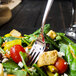 A Walco stainless steel salad fork in a salad with croutons and vegetables.