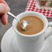 A hand holding a Walco Pacific Rim stainless steel demitasse spoon over a cup of coffee.