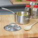 A Vollrath stainless steel sauce pan filled with soup and a wooden spoon.