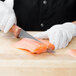 A person using a Mercer Culinary Praxis stiff boning knife to cut a piece of salmon.