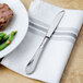 A Walco stainless steel dinner knife on a white napkin next to a plate of steak and green beans.