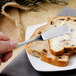A person using a Walco stainless steel butter knife to spread butter on a piece of bread.