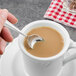 A hand holding a Walco Meteor stainless steel demitasse spoon in a cup of coffee.