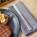 A Walco Bosa Nova dinner knife on a napkin next to a plate of barbecued meat.