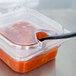 A Carlisle clear plastic container with a black spoon in it.