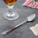 A Walco Meteor iced tea spoon next to a glass of liquid on a table.
