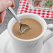 A hand holding a Walco stainless steel demitasse spoon in a cup of coffee.