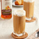 A bottle of Monin Zero Calorie Natural Caramel Flavoring Syrup next to a glass of iced coffee with foam and a spoon.