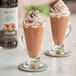 Two glasses of chocolate milkshakes with whipped cream and Monin Zero Calorie Natural Chocolate Flavoring Syrup on a table.