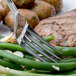 A Walco stainless steel dinner fork holding meat and green beans on a plate.