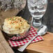 A Walco Bosa Nova teaspoon next to a bowl of mashed potatoes on a table.