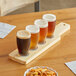 A wooden paddle holding four Barbary tasting glasses of beer on a table