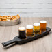 A Libbey melamine flight paddle with a row of beer glasses on it and a tray of pretzels.