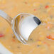 A Walco stainless steel bouillon spoon in a bowl of soup.