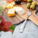 A Walco Barony stainless steel cocktail fork on a cutting board with cheese and olives.