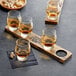 A Reserve by Libbey Kentucky Bourbon Trail Tasting Flight on a wooden board with brown liquid and nuts.