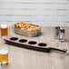 A Libbey Cherry Wood melamine flight paddle with three beer holders on a table with a glass of beer.