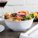 A bowl of salad with onions and croutons in a white Thunder Group melamine swirl bowl.