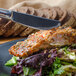 A Walco Barony stainless steel dinner knife slicing salmon on a plate.