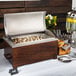 A buffet with a mahogany wood chafer stand on a table filled with food in a container.