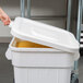 A hand opening a white Continental Huskee square trash can lid.