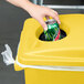 A hand putting a can into a yellow Rubbermaid Slim Jim trash can with 2 hole lid.