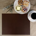 A H. Risch Inc. mahogany faux leather rectangle placemat on a table with coffee and pastries.