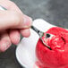 A hand holding a Fineline silver plastic tasting spoon over a scoop of red ice cream.