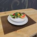 A light brown rectangular woven vinyl placemat with a plate of fruit on a table.
