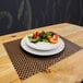 A plate of salad with fruit on a bronze and brown woven vinyl rectangle placemat.