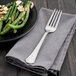 A Walco stainless steel table fork on a napkin next to a plate of green beans and almonds.