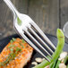 A Walco Prim stainless steel table fork on a plate of salmon and green beans.